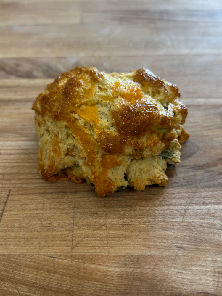 jalapeno cheddar scone | JustDane | Changing Lives. Changing the Community Golden-brown cheese biscuit resting on a wooden cutting board.