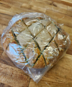 Round loaf of stuffed bread cut into square wedges and wrapped in plastic on a wooden surface.