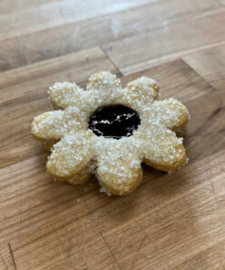 Flower-shaped pastry with sugar crystals and a dark jam-filled center on a wooden board.