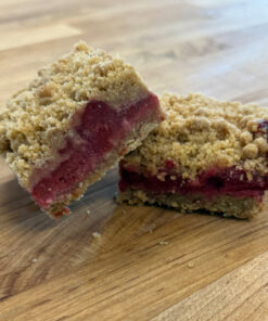 Two berry crumble bars on a wooden cutting board, showing a red jam-filled center and a crumbly streusel topping.